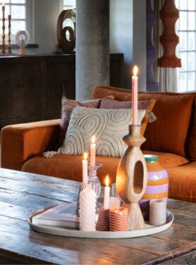 Hoge houten kandelaar op rond dienblad met roze accessoires