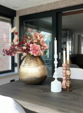 Gouden bolvaas met roze kunstbloemen en roze kandelaren op tafel
